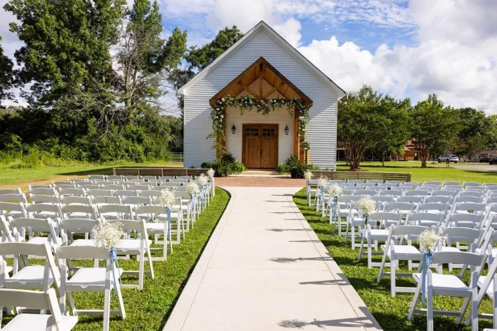 Ceremony aisle lined with white chairs leading to the white chapel at Alvastage Acres